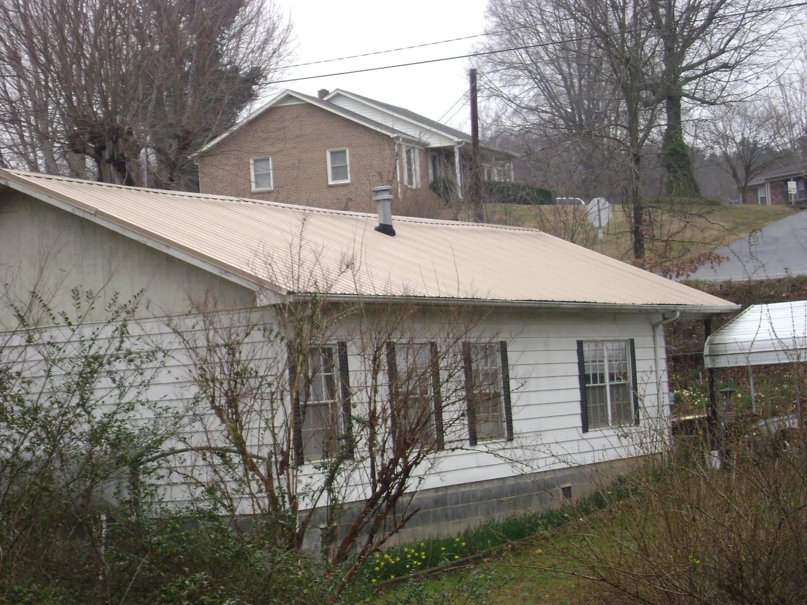 Tan metal roof on a white sided house set into a hillside — Commercial Roofing by Roofing Brothers in Sandy Hook